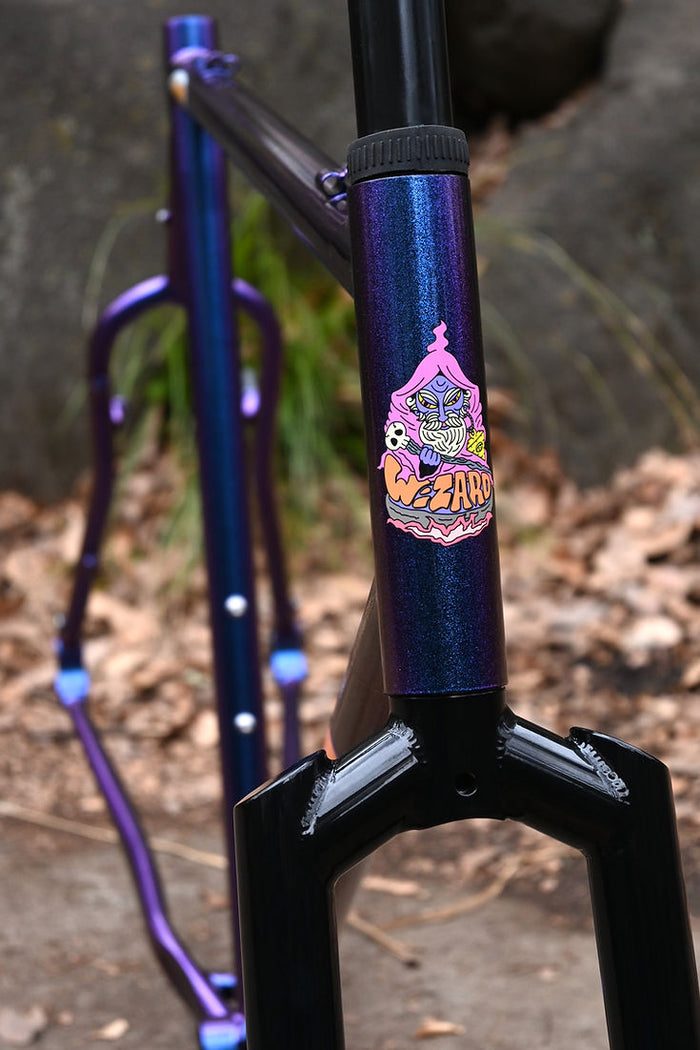 Head tube detail: a pink wizard decal and the Wizard wordmark in flat orange, on the purple-to-blue flip sparkle paint